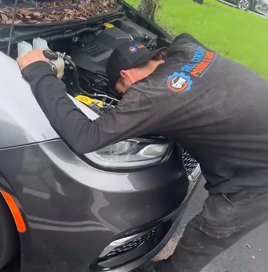 All County mobile mechanic working under the hood of a customer's car in their driveway